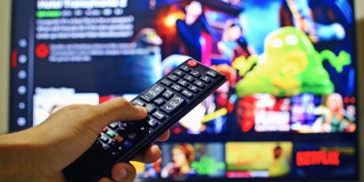 person holding remote control to a TV showing Netflix