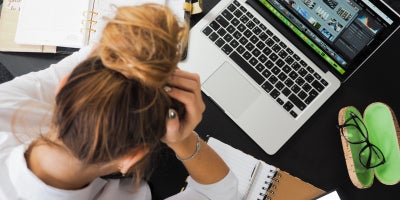 top view of woman working on laptop with notebooks and head in her hands