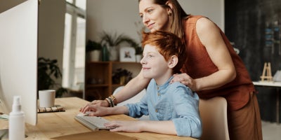 a parent looks at the computer screen with child over the shoulder