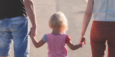 child holds hands with two adults