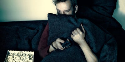 Man watches TV hiding behind pillow