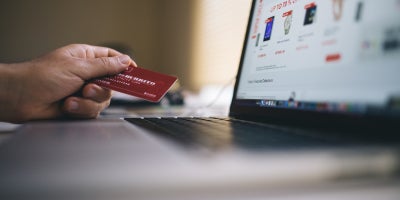 image of person holding credit card next to laptop with shopping site
