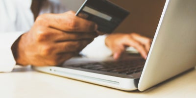 man shops online at laptop with credit card in hand