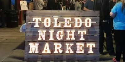photo of wooden sign with words toledo night market in lights
