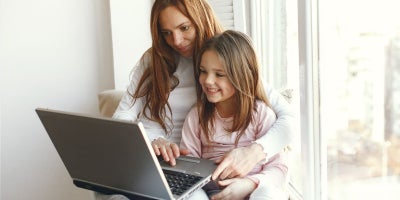 mother and daughter sit in a windowsill using a laptop, back to school laptop