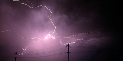 Lightning against a purple-colored sky positioned behind power lines 