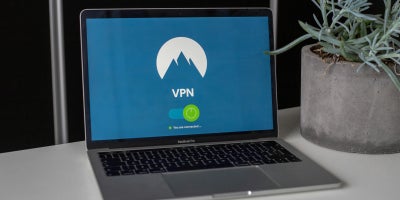 Laptop computer on desk next to a house plant with the screen display showing “VPN” with the logo of a mountain in the background.