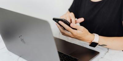 Woman on cellular phone sitting in front of an Apple MacBook on top of a granite tabletop