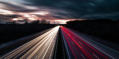 Two-way road with red and white lights shining over them with cloudy skies in the background