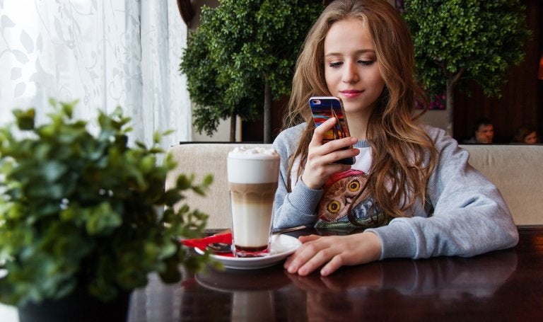 young girl sits at cafe table with drink while looking at her cell phone