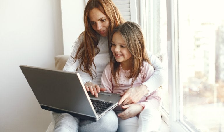mother and daughter sit in a windowsill using a laptop