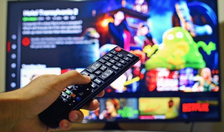 person holding remote control to a TV showing Netflix