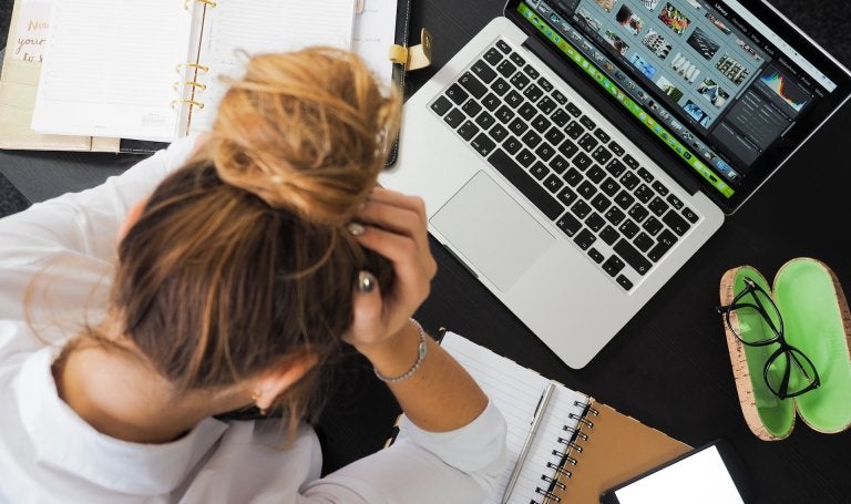 top view of woman working on laptop with notebooks and head in her hands