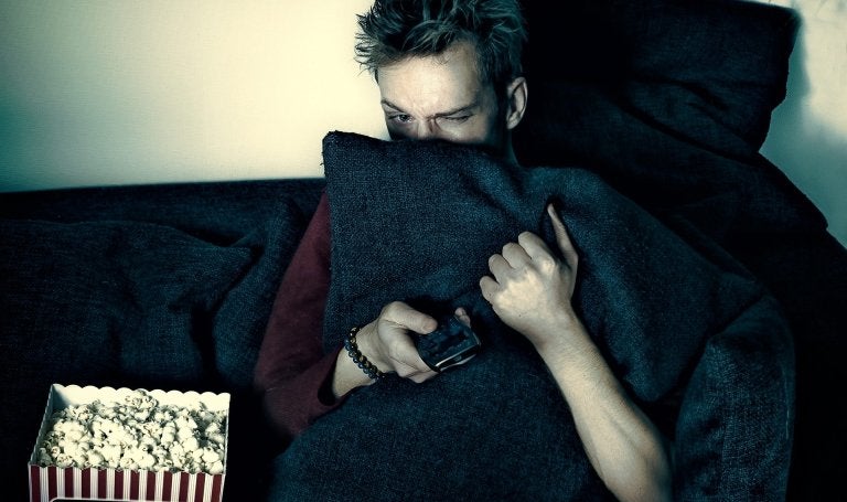 Man watches TV hiding behind pillow