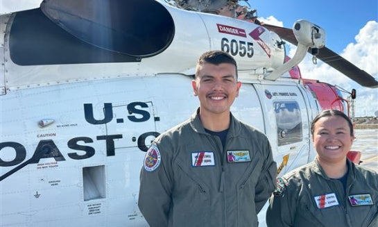 This photo made with a smartphone shows U.S. Coast Guard officer Josh Law, left, and lieutenant Miyako Miller standing in front of a rescue helicopter at the U.S. Coast Guard Air Station in Ventura, Calif., on Oct. 22.