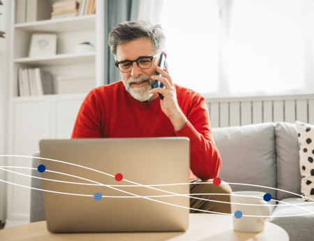 Man sitting on a couch, talking on phone, and using laptop