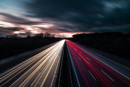 Two-way road with red and white lights shining over them with cloudy skies in the background