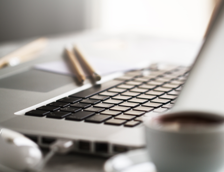 close-up image of a laptop keyboard with a coffee cup on a table