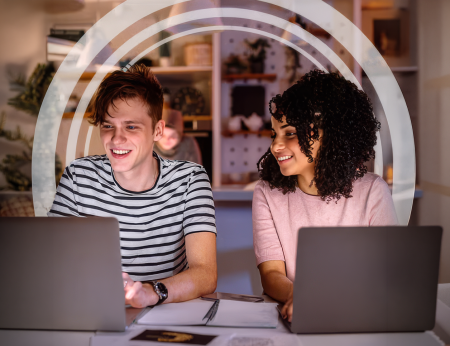 smiling college students using laptops sitting at a table