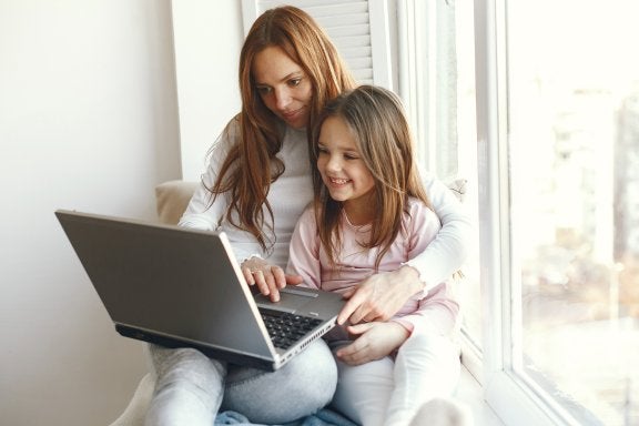 mother and daughter sit in a windowsill using a laptop