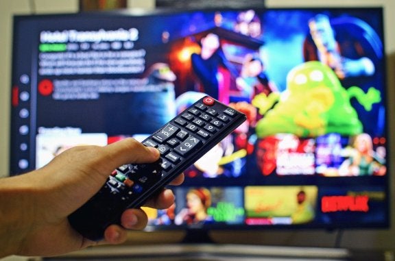 person holding remote control to a TV showing Netflix