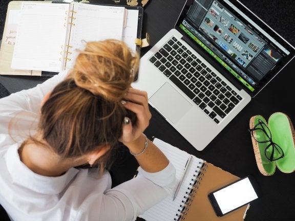 top view of woman working on laptop with notebooks and head in her hands