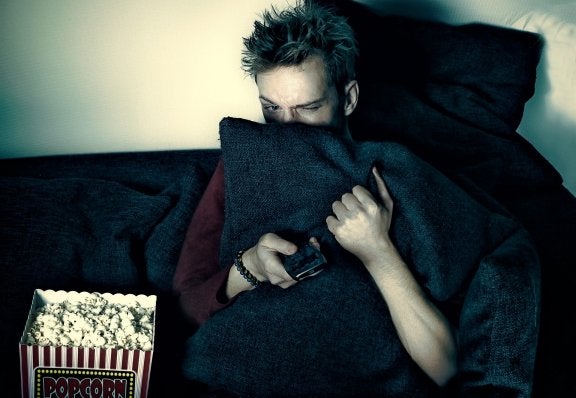 Man watches TV hiding behind pillow