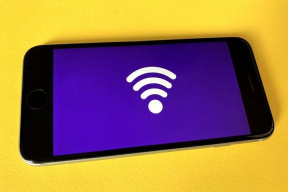 cell phone with a wifi symbol displayed laying on yellow table, blog, need more internet speed