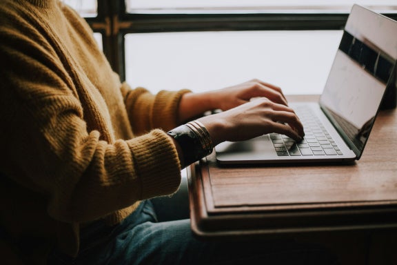 Person sitting next to a window while working on a laptop computer