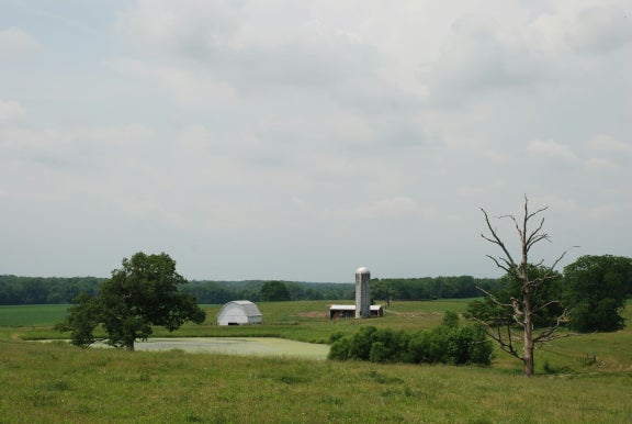 Rural landscape with barn showing and greenery with a cloudy background.