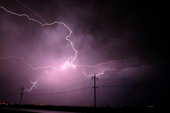Lightning against a purple-colored sky positioned behind power lines 