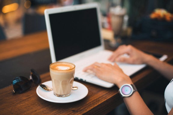 Woman working on laptop with a coffee at a table using public WiFi