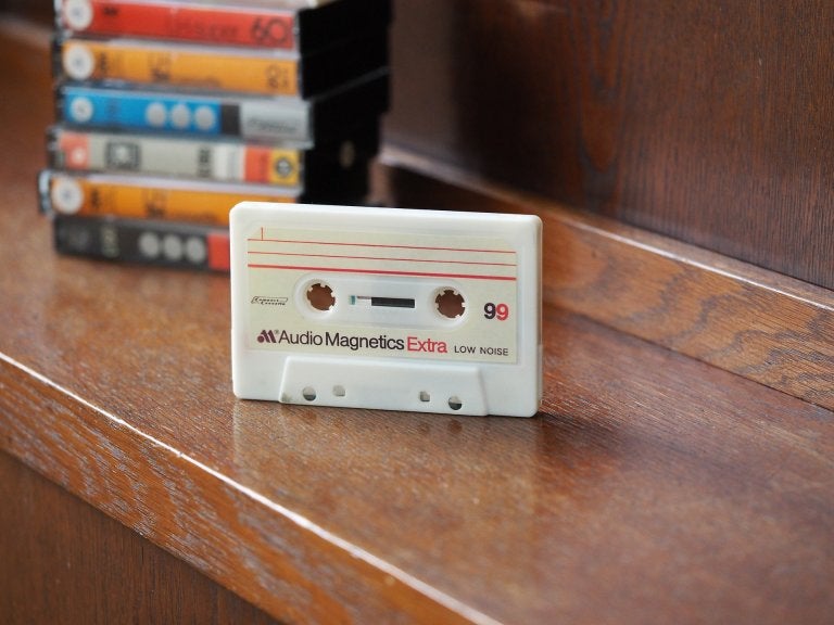 photo of cassette standing upright on table with stack of cassette cases behind 