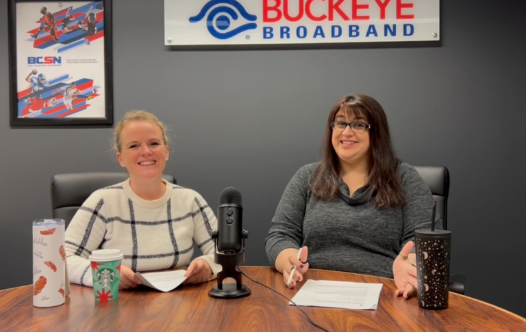 kim, blonde and smiling, sits next to rani, brunette and happy, under the buckeye broadband logo with a mic on the table