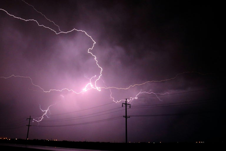 Lightning against a purple-colored sky positioned behind power lines 