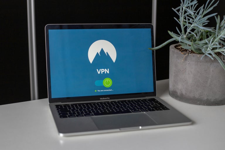 Laptop computer on desk next to a house plant with the screen display showing “VPN” with the logo of a mountain in the background.