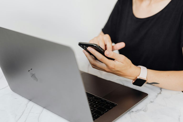 Woman on cellular phone sitting in front of an Apple MacBook on top of a granite tabletop