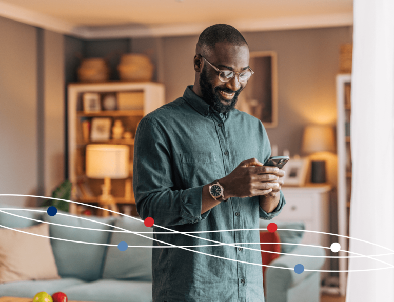 Man standing in living room typing on his phone and smiling