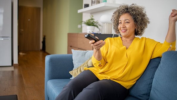 Woman in yellow shirt on couch with remote in hand image, internet and cable tv bundle, internet bundle, cable tv bundle, tivo+